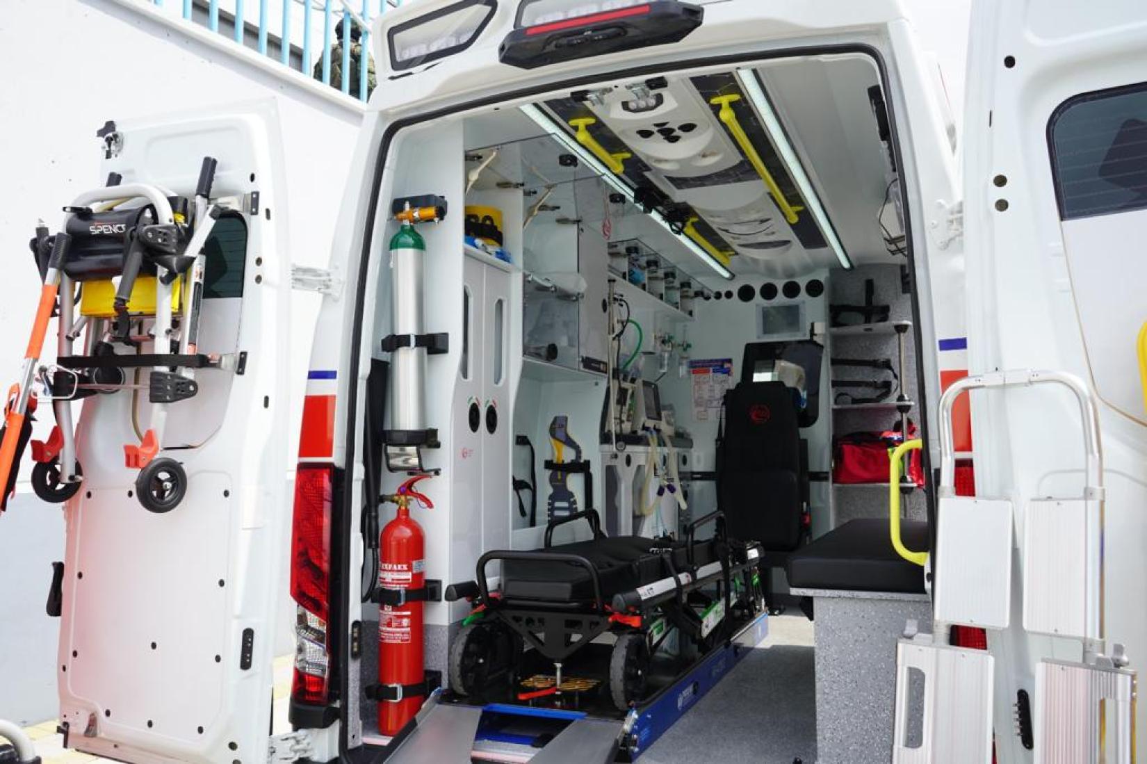 Interior de una de las ambulancias entregadas al Ministerio de Salud Pública. Se puede apreciar a la ambulancia con la puerta abierta, y dentro de ella una camilla, un extintor y equipamiento médico moderno.